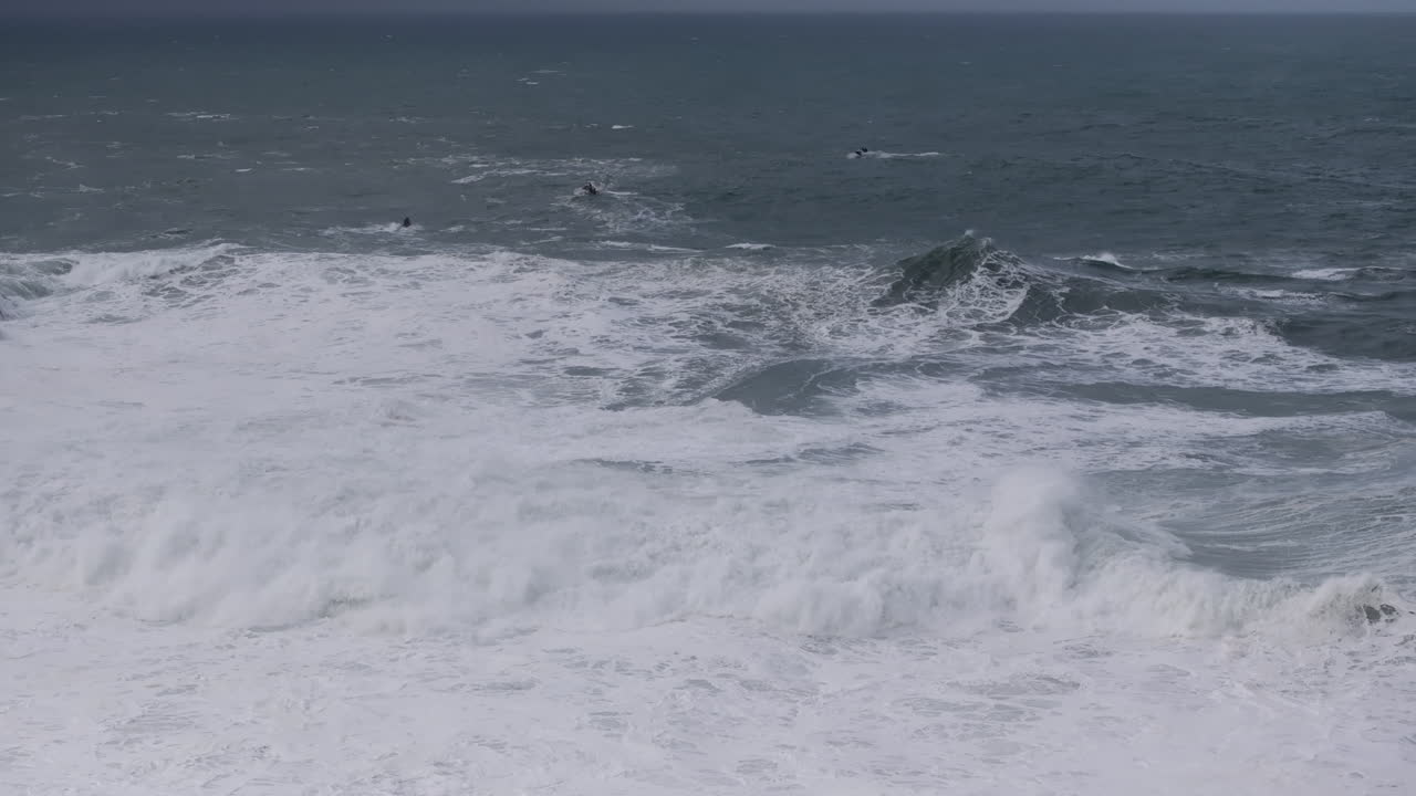 Jet ski teams approaching winter powered Nazaré waves. Aerial drone shot, Portugal, Europe