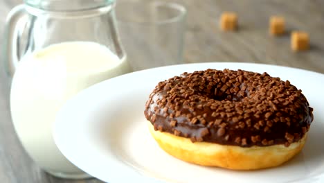 delicious sweet donut with chocolate icing rotating on a plate. rustic wooden table. looped