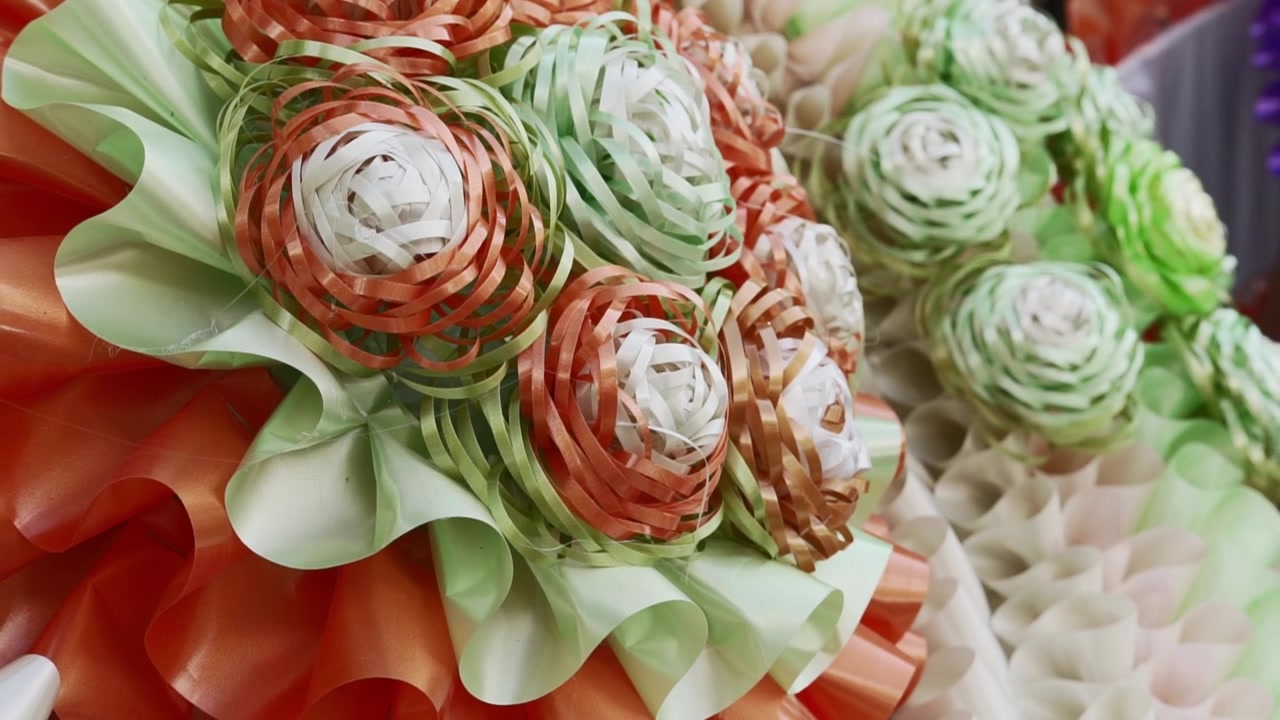 Close-up of colorful paper flowers and ribbon decorations for Día de Muertos, showing handmade Mexican craft details in soft focus.