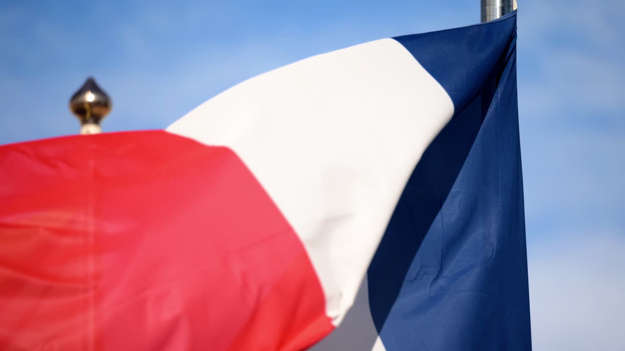 Close up of the flag of France waving in the wind with a blue sky on the background