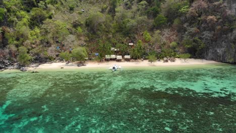 aerial tilt drone shot flying over clear, shallow, blue water and tilting down towards a paraw boat at a private beach, at coron island, in philippines, asia