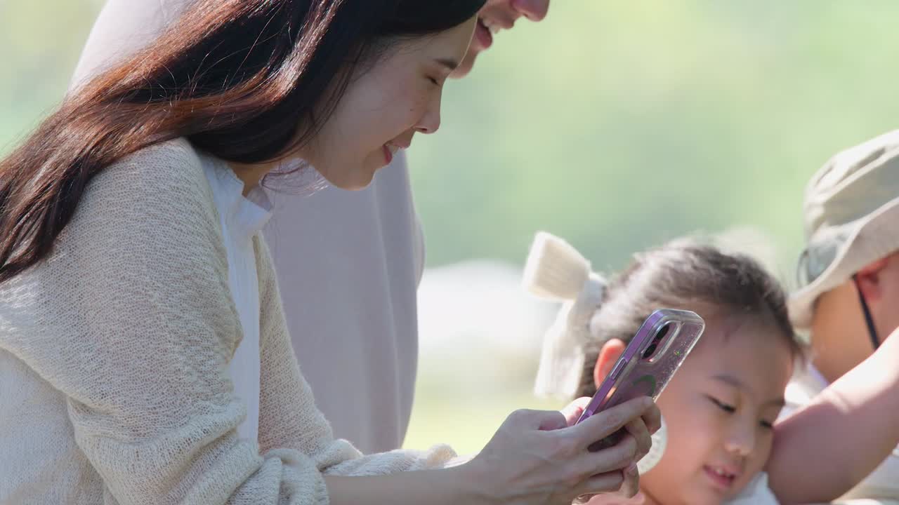 행복한 아시아 가족이 스마트폰을 함께 보면서 웃고 하트 모양을 만들고 있어요