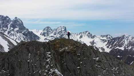 Cinematic-rotating-drone-shot-of-hiker-standing-on-top-of-a-mountain-ridge-in-the-snow-covered-Caucasus-Mountains-in-Georgia