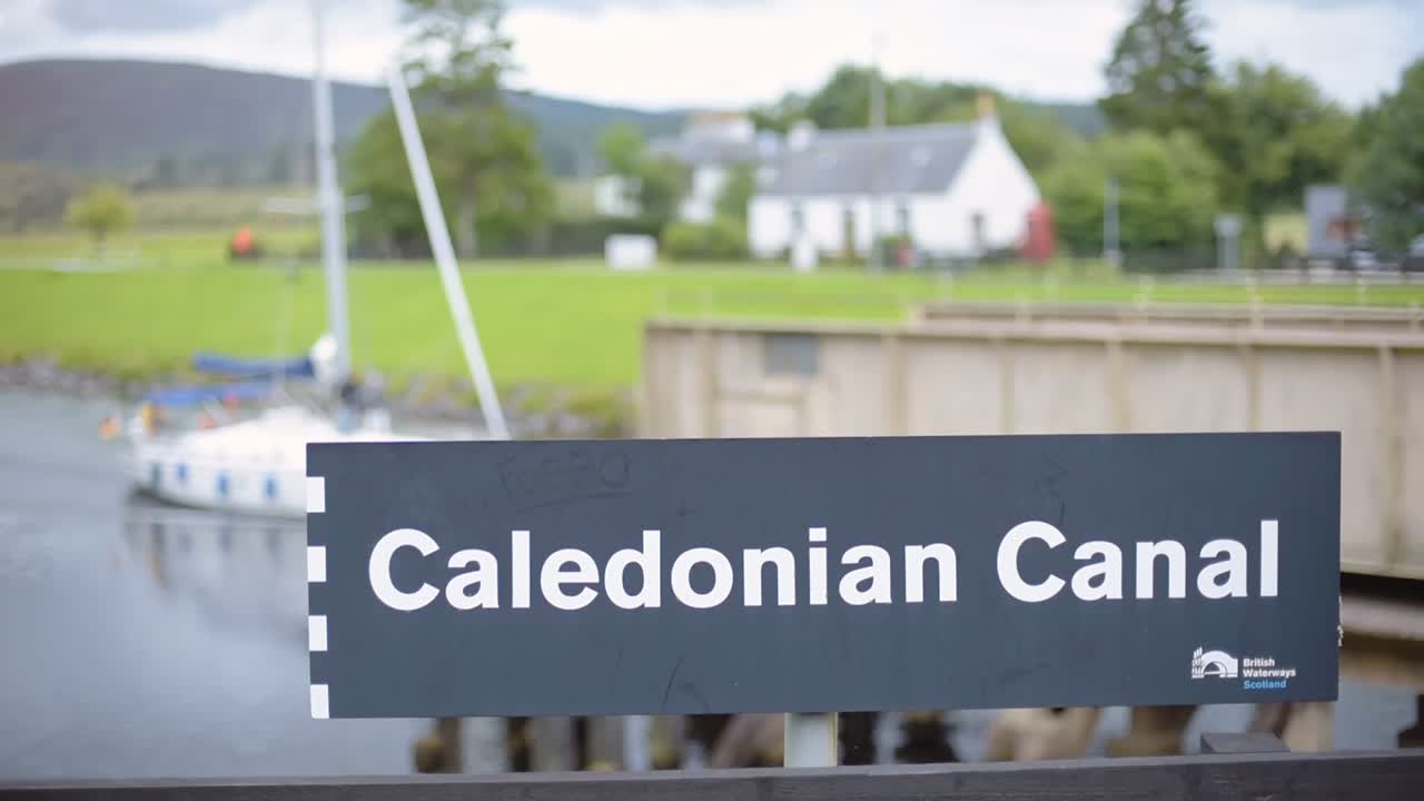 Caledonian Canal sign, Scotland, with sailboats passing by in the background