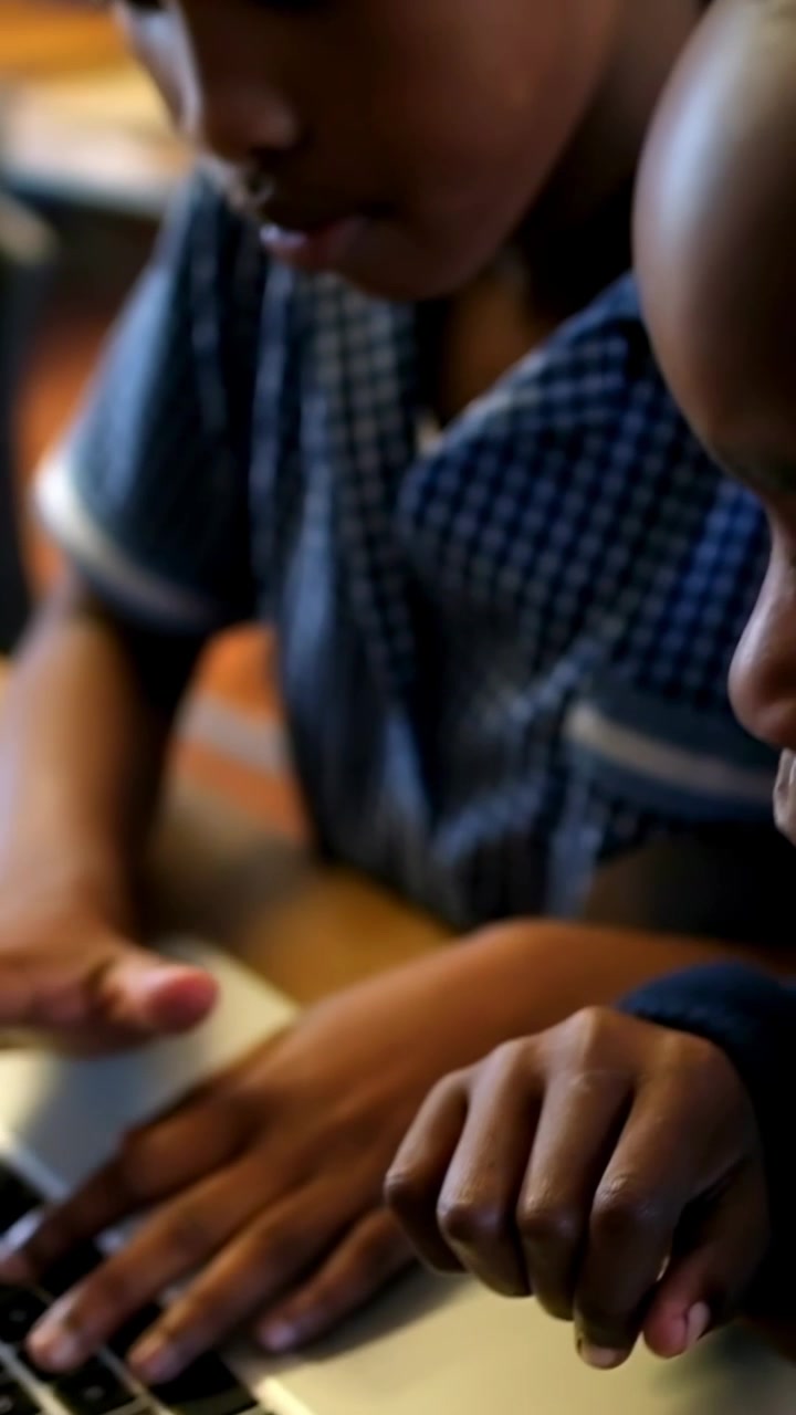 Vertical video: Placing palms child in blue checked shirt typing, working on silver laptop on table
