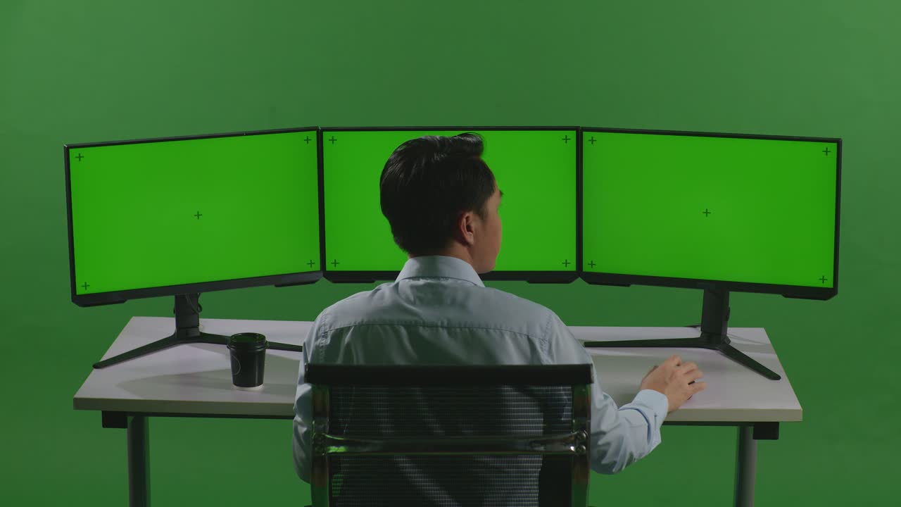 무언가에 대해 생각하고 있는 아시아 남자의 뒷면, 그 다음에는 녹색 스크린 스튜디오에서 여러 컴퓨터 모니터를 모의로 작업하는 동안 지표손가락을 들어 올립니다.