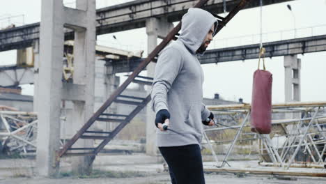 caucasian man with beard in a grey hoodie jumping rope outdoors an abandoned factory on a cloudy morning