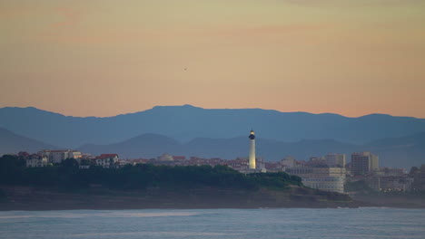 Cinematográfico-Impresionante-Todavía-De-Cerca-Dramático-Brillante-Naranja-Nubes-Puesta-De-Sol-Oscuridad-Faro-Pájaro-Volando-Biarritz-Hossegor-Francia-Playa-Montaña-Paisaje-Costero-Biarritz-País-Vasco-Bahía-De-Aguas-Tranquilas