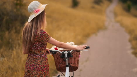 Lens-flare:-smiling-happy-woman-in-short-dress-is-riding-a-bicycle-with-a-basket-and-flowers-in-the-park-with-green-trees-around-during-the-dawn.-Slowmotion-shot