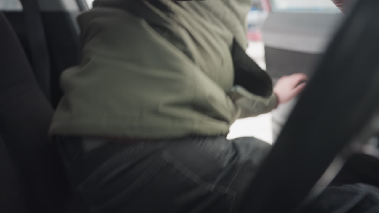close up of driver in winter jacket stepping out of parked vehicle with interior partially visible and snowy urban background outside window, capturing natural motion and cold season environment