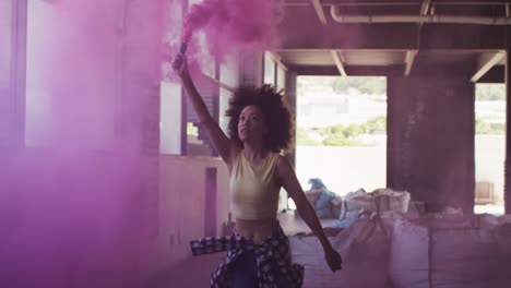 Mixed-race-woman-holding-purple-flare-running-through-an-empty-building