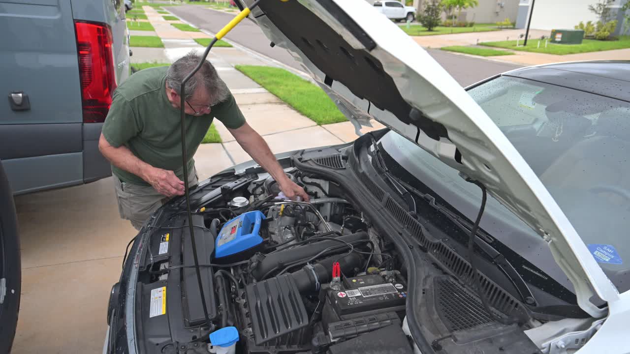 hombre mayor limpia el compartimento del motor de su coche mientras espera que una batería se cargue