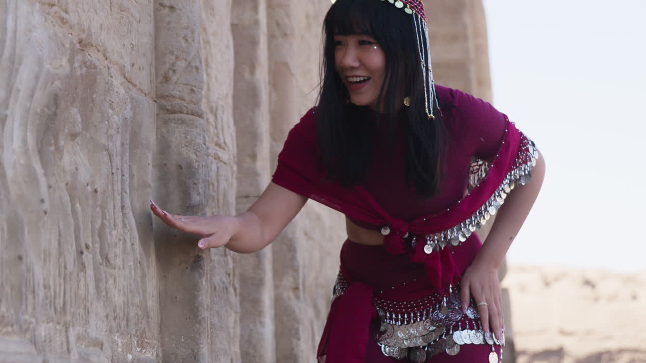 Woman in traditional dress interacting with ancient temple wall in Dendera