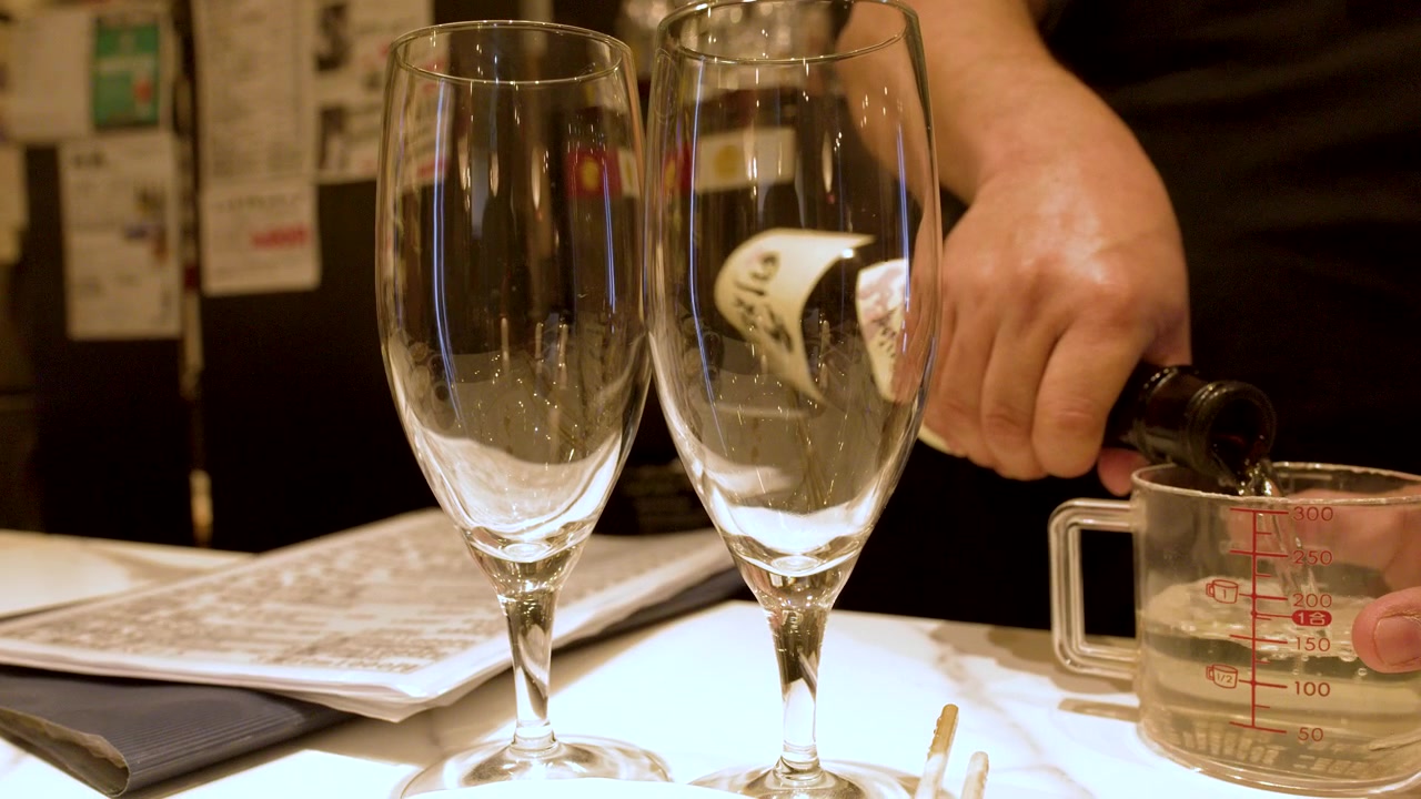 Un primo piano mostra del sake versato da una bottiglia in un misurino di vetro.