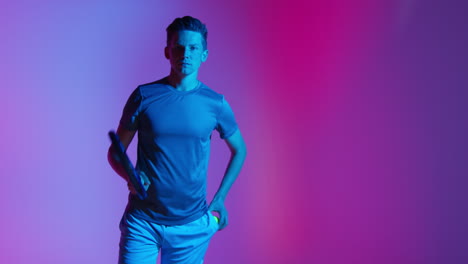 Studio-Portrait-Of-Male-Tennis-Player-Bouncing-Ball-On-Racket-Preparing-To-Serve-Against-Low-Key-Colourful-Mixed-Lighting