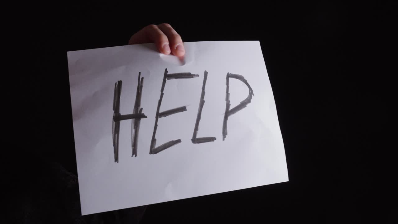 Hand turning a “help” sign toward the camera, symbolizing reaching out and asking for support