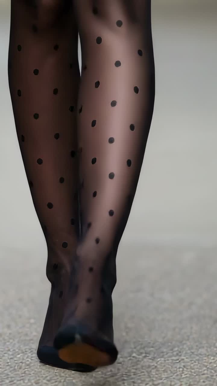 Vertical video: Walking model's legs stepping on runway showing sheer dot tights short skirt pumps