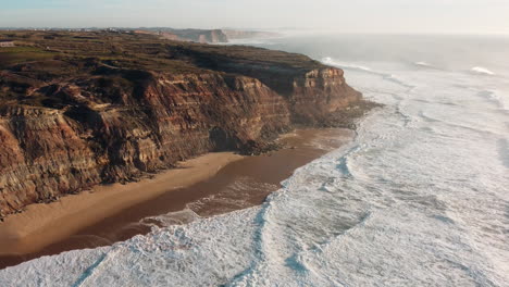 aerial of south imposing cliffs rising straight up from the beach, rugged and scenic headland coast of portugal, the westernmost point in continental europe