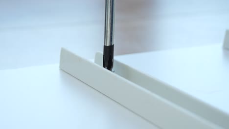 primer plano de un destornillador apretando un tornillo en una parte de plástico blanco