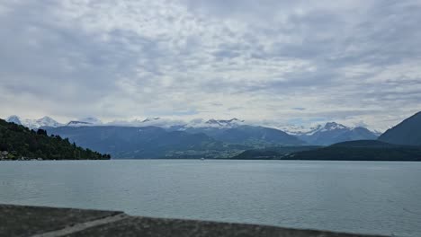 Static-time-lapse-shot-of-overcast-Swiss-lake-Thun-with-mountains-in-background-and-boat-on-water