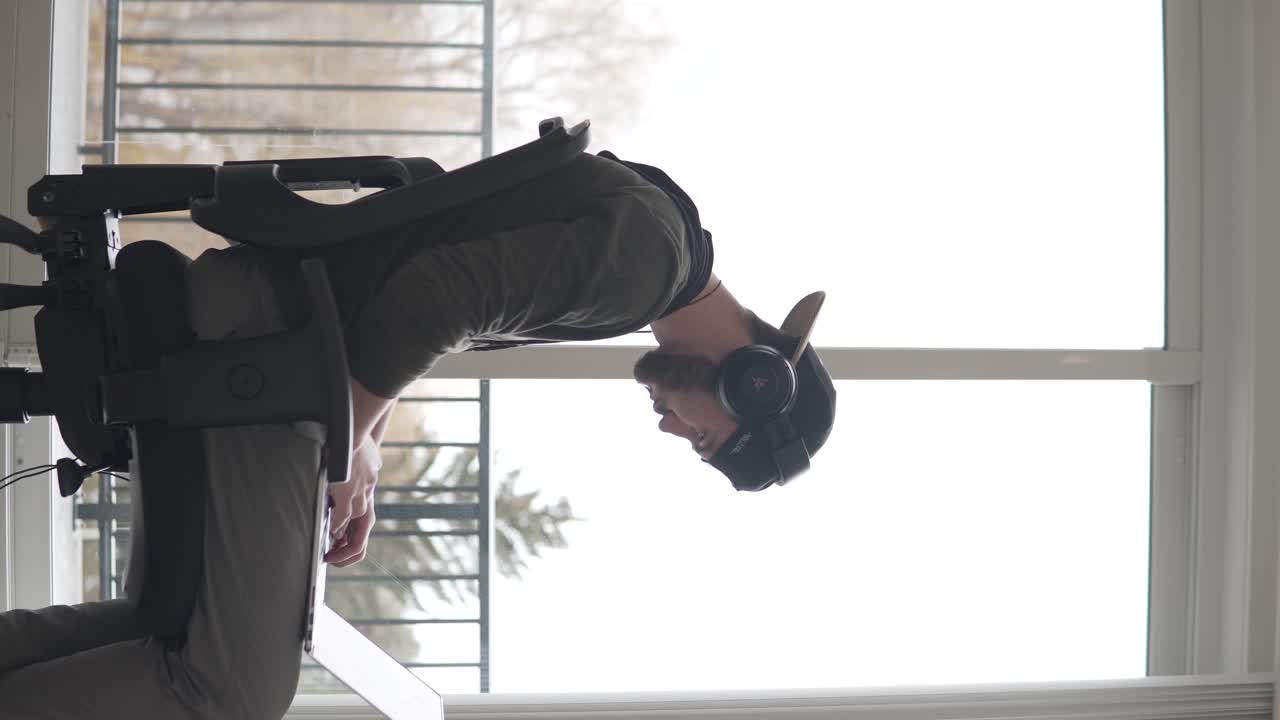 Vertical Video, Profile of Young Male, Music Producer or Freelancer With Laptop and Headphones Working in Rhythm of Music in Bright Living Room, Static Shot