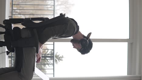 video vertical, perfil de hombre joven, productor musical o autónomo con laptop y auriculares trabajando al ritmo de la música en una sala de estar luminosa, tiro estático