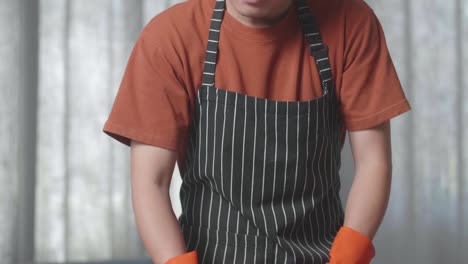 close up of asian male housekeeper with an apron enjoys vacuuming the floor at home