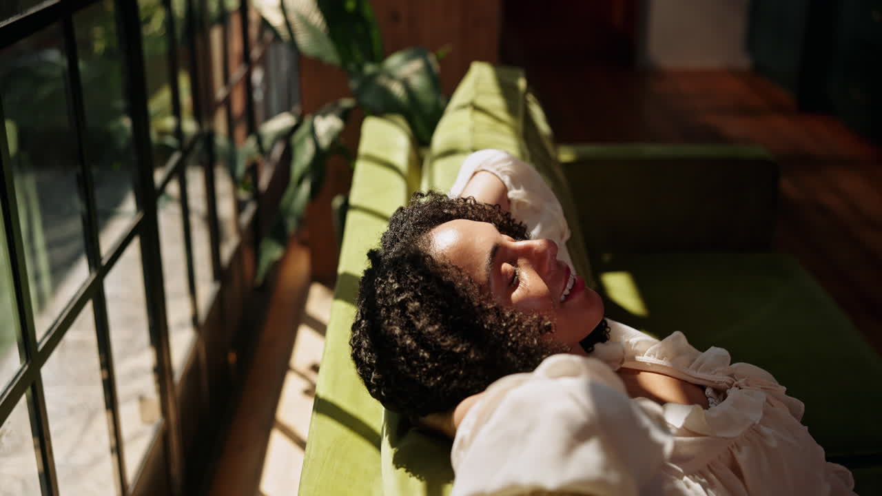 Giovane donna con i capelli ricci che si rilassa sul divano alla luce del sole