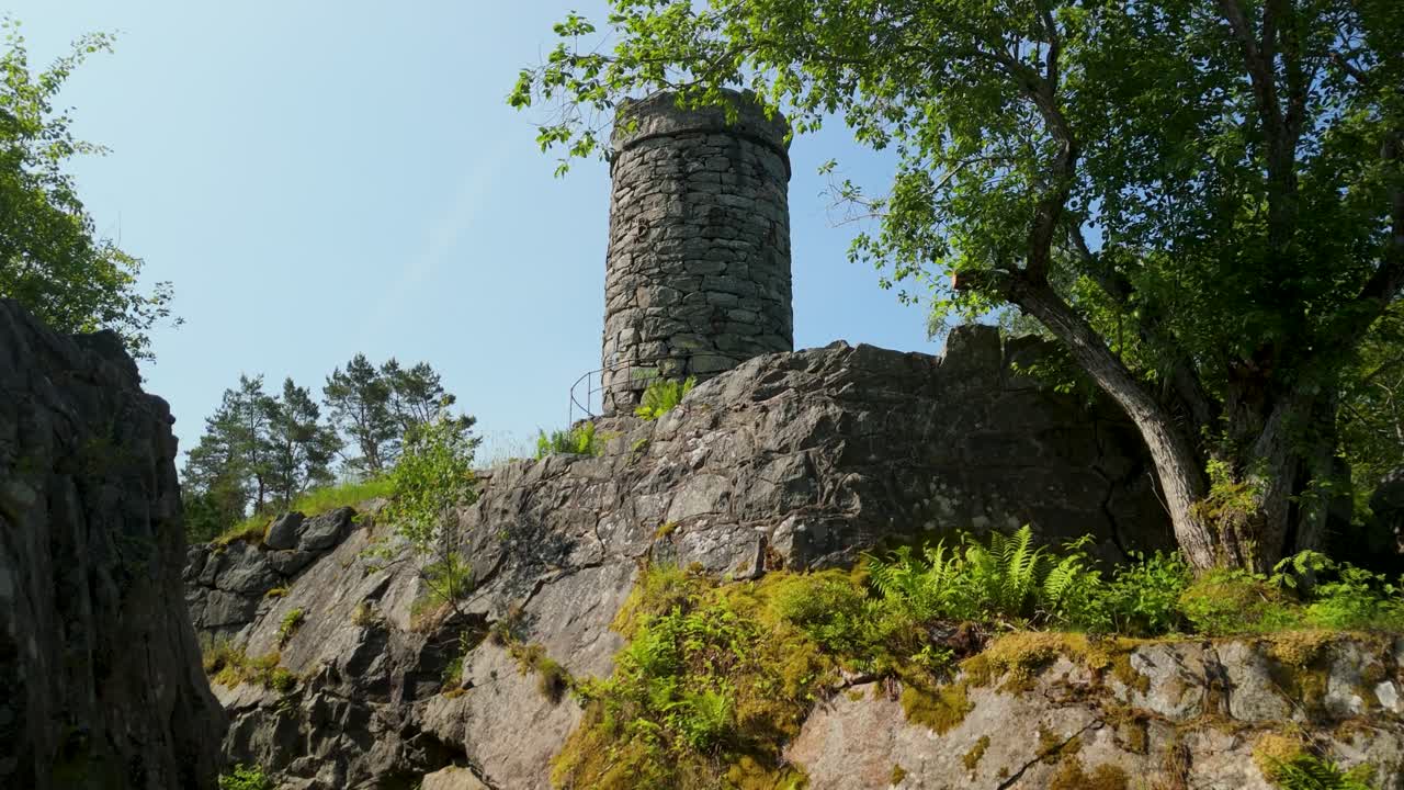 Vista aérea volando a través de un arco de piedra cubierto de musgo que revela la torre redonda medieval de Tureborg Slott encaramada sobre rocas de granito en Uddevalla, Suecia.