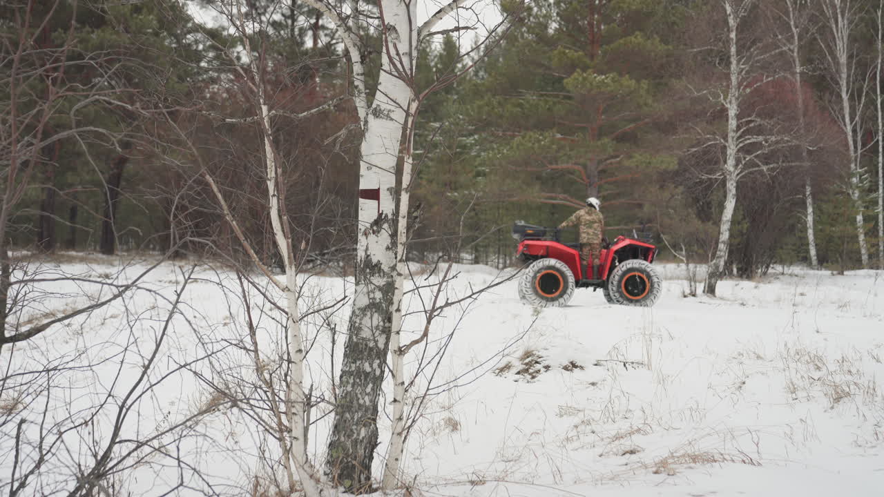 Pilota di ATV rosso in una foresta di betulle innevata. Primo piano di un singolo pilota che naviga un sentiero stretto. Ruggito del motore e ruote che girano sollevando neve. Atmosfera invernale tesa, mani sull'acceleratore. Pieno di adrenalina.