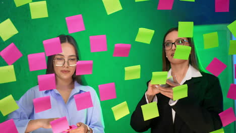 dark-haired women put the colorful bright sticky notes on the glass board. planning, memo notes creation.