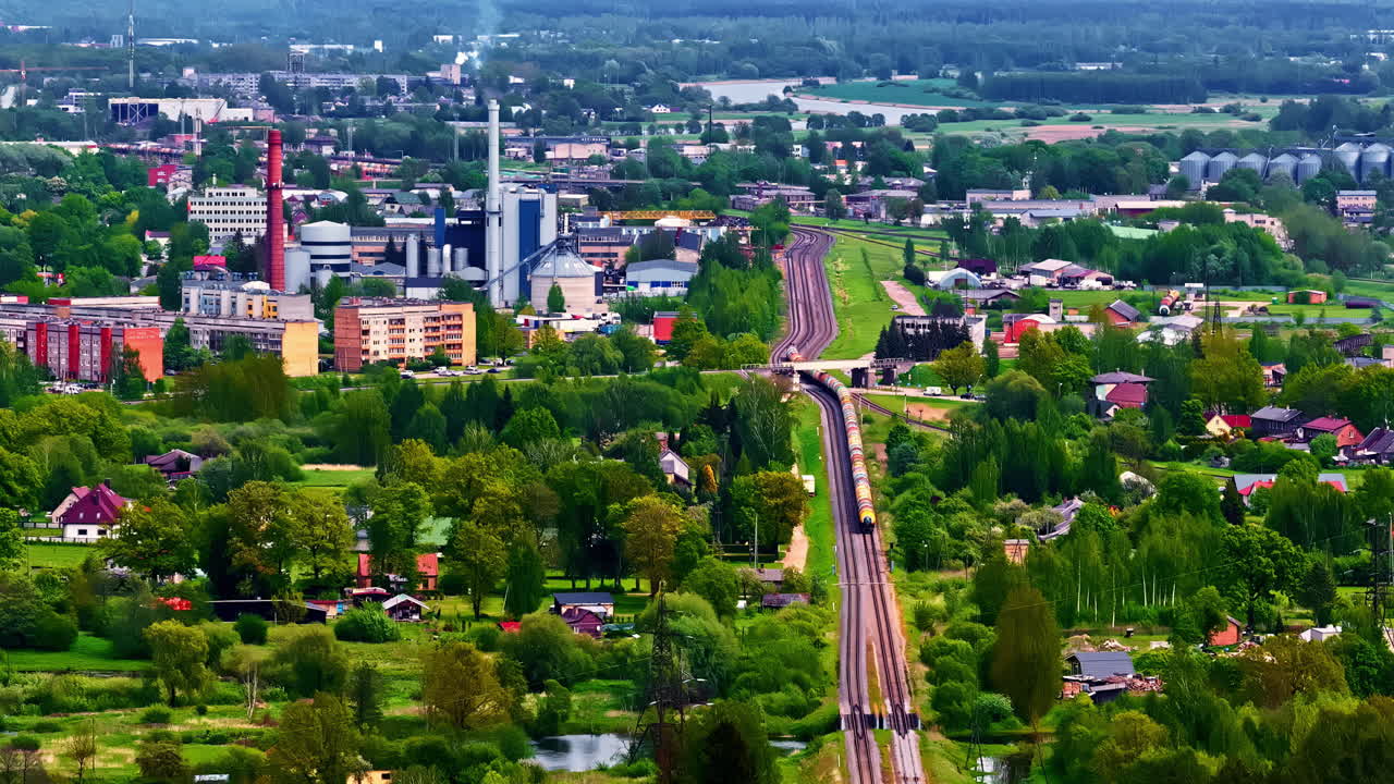 Aerila hyperlapse of freight train approaching city through trees and residential suburbs