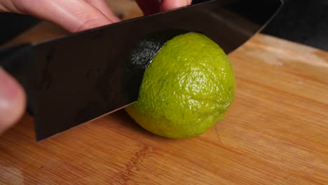 cutting a fresh, juicy lime in half with black knife on wooden cutting board