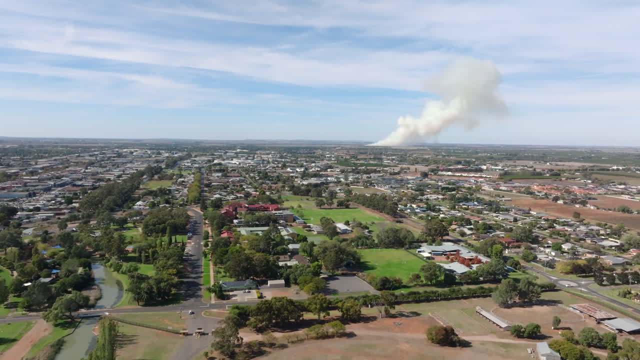 Drone shot of Griffith town and smoke from agriculture field burning in the distance, NSW Australia