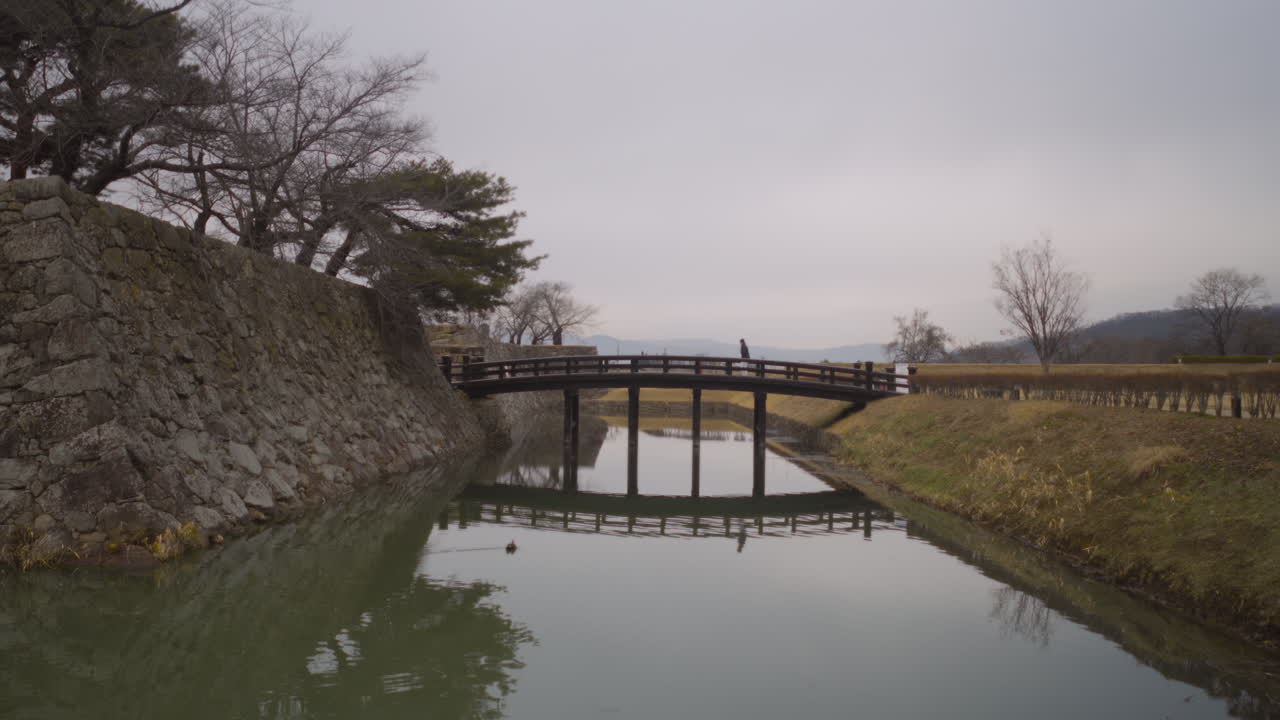 Man walks on a wooden bridge over a molt, Kawanakajima Battleground, Japan