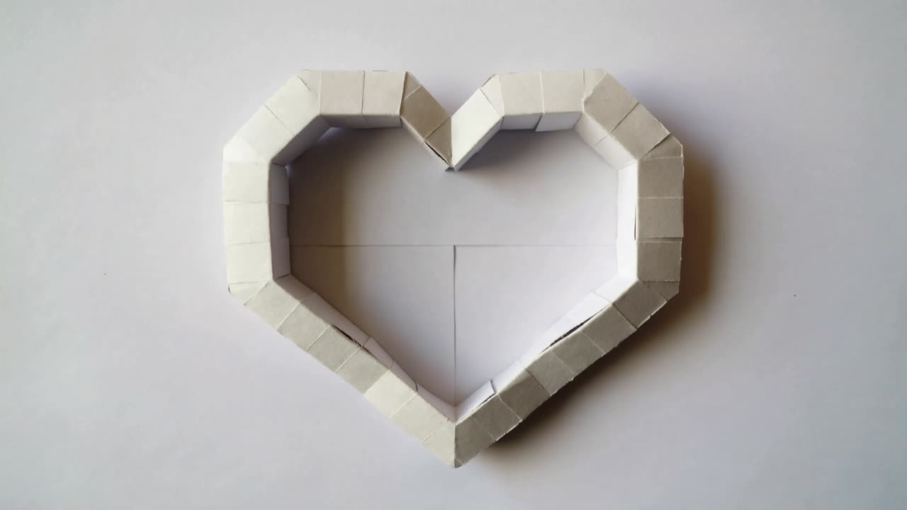 Recording folded heart paper frame staying centered on white sheet, showing crease lines, shadows