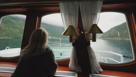 a woman looks out of the porthole at the beautiful scenery of norway floats on a ship on the norwegi