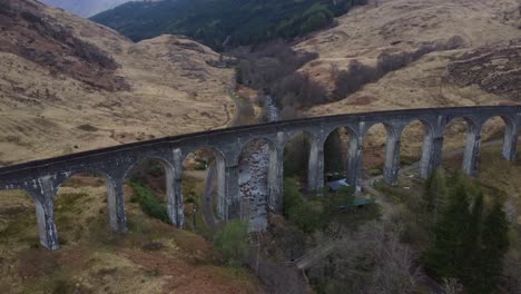 Iconic Glenfinnan Viaduct with drone tilt up to reveal landscape behind in Autumn