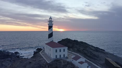 Sunset-outlining-the-Favaritx-lighthouse-in-Menorca-Spain-with-rocky-cliff-top-edges-surrounding-the-structure