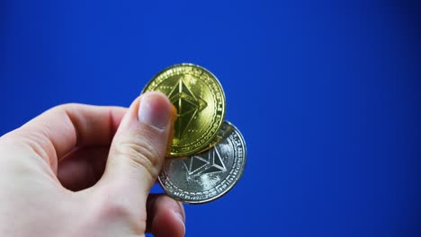 A close-up of a hand shifting gold and silver Ethereum coins, reflecting on blue background