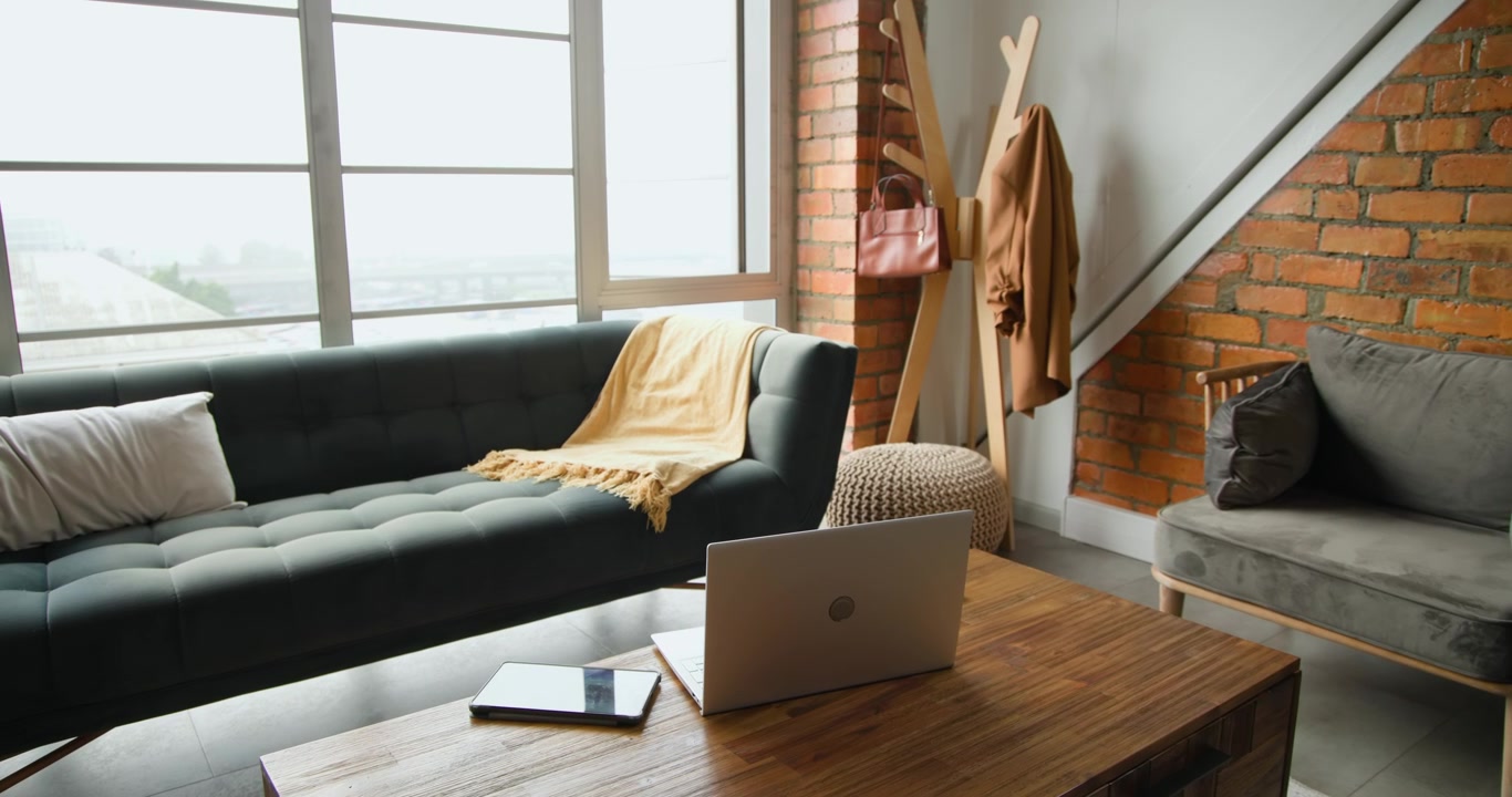 La telecamera inizia a panoramare a destra, rivelando un tavolino da caffè in legno con un laptop aperto per una ripresa di uno spazio di lavoro.