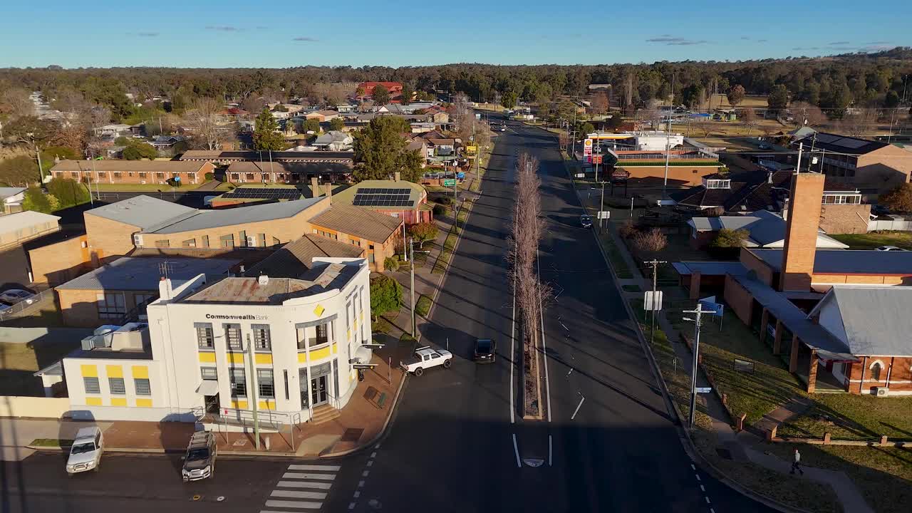 Aerial tracking shot of a single car driving along a quiet urban street in a small Australian town, with late afternoon sunlight and clear skies
