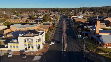 aerial tracking shot of a single car driving along a quiet urban street in a small australian town, with late afternoon sunlight and clear skies