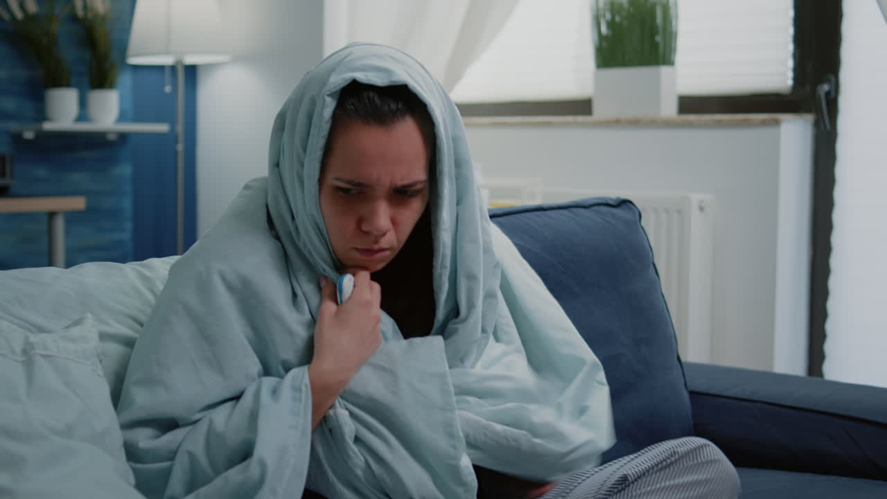 Person wrapped in blanket using thermometer