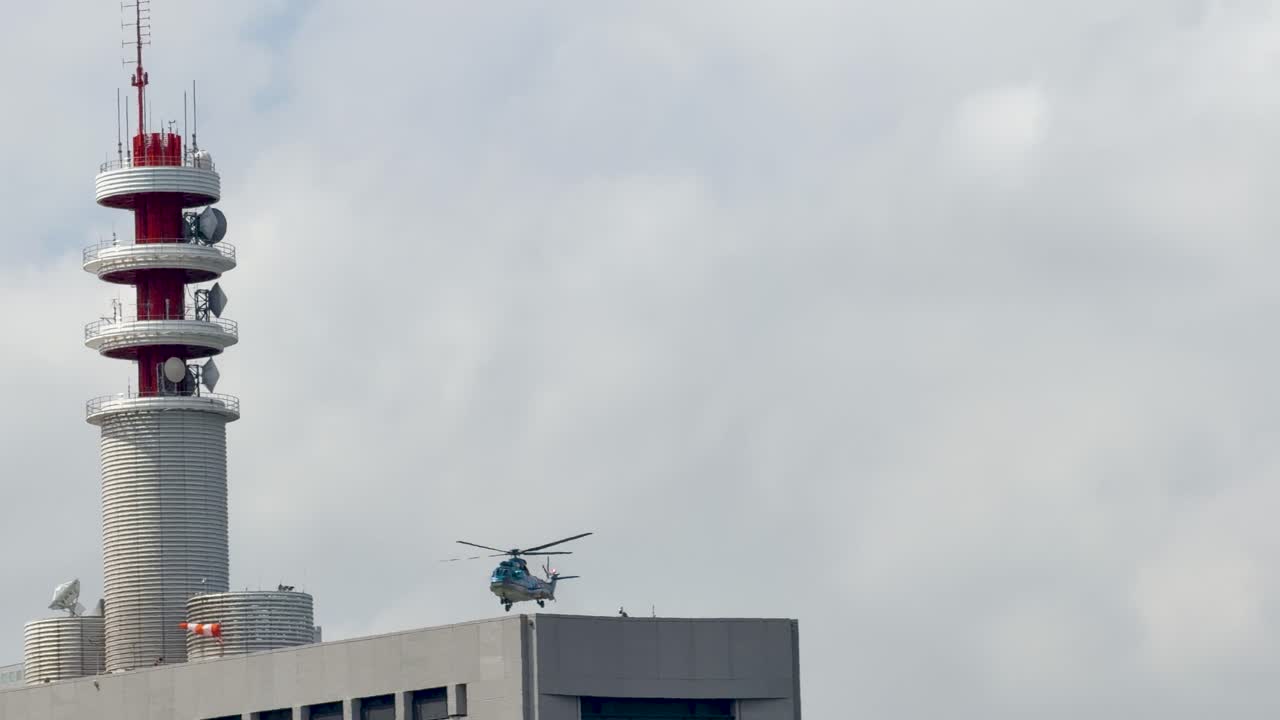 Et helikopter lander på en helikopterplass på taket av en bygning ved siden av et høyt kommunikasjonstårn i Tokyo