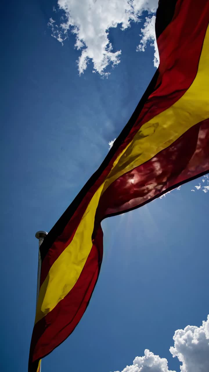 Low-angle shot of a flag waving against a bright blue sky with clouds, capturing the sunlight