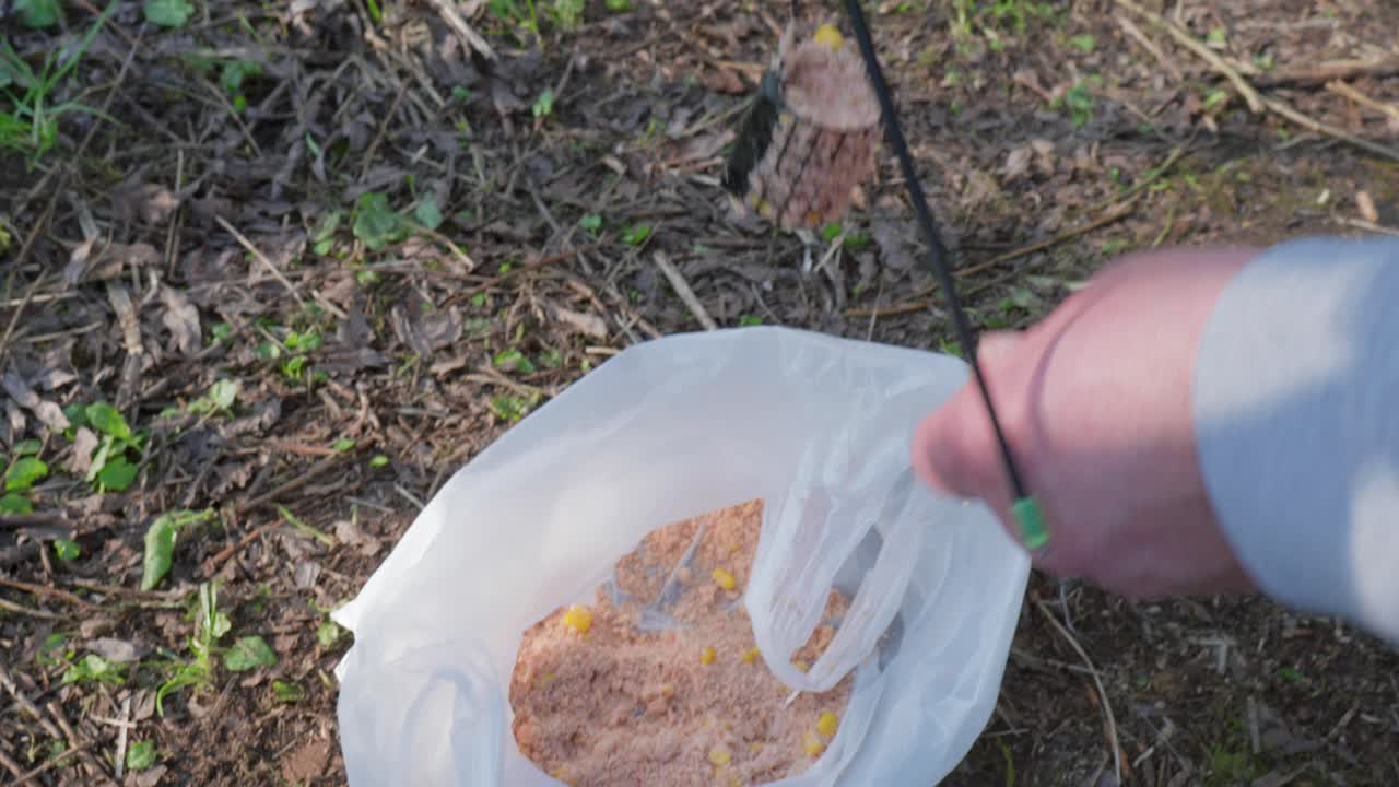 Hands preparing bait for fishing in a forested area with a plastic bag