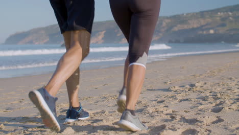 man and woman in sportswear and sneakers running on sandy beach