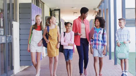 portrait of diverse female teacher and happy schoolchildren walking in school