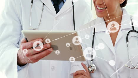 animation of network of people icons over smiling caucasian female and male doctor using tablet